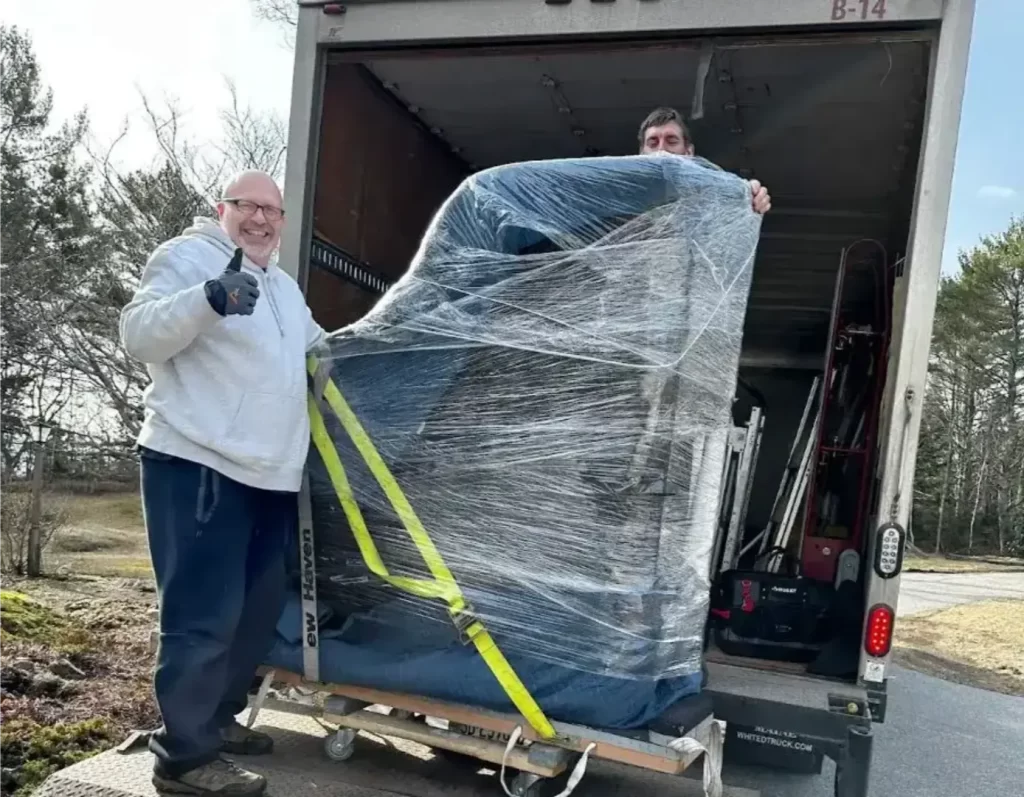 Two movers loading wrapped furniture.