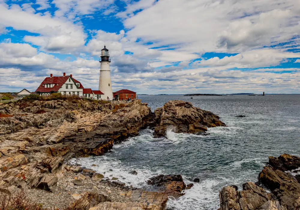 Lighthouse by rocky coastline under clouds